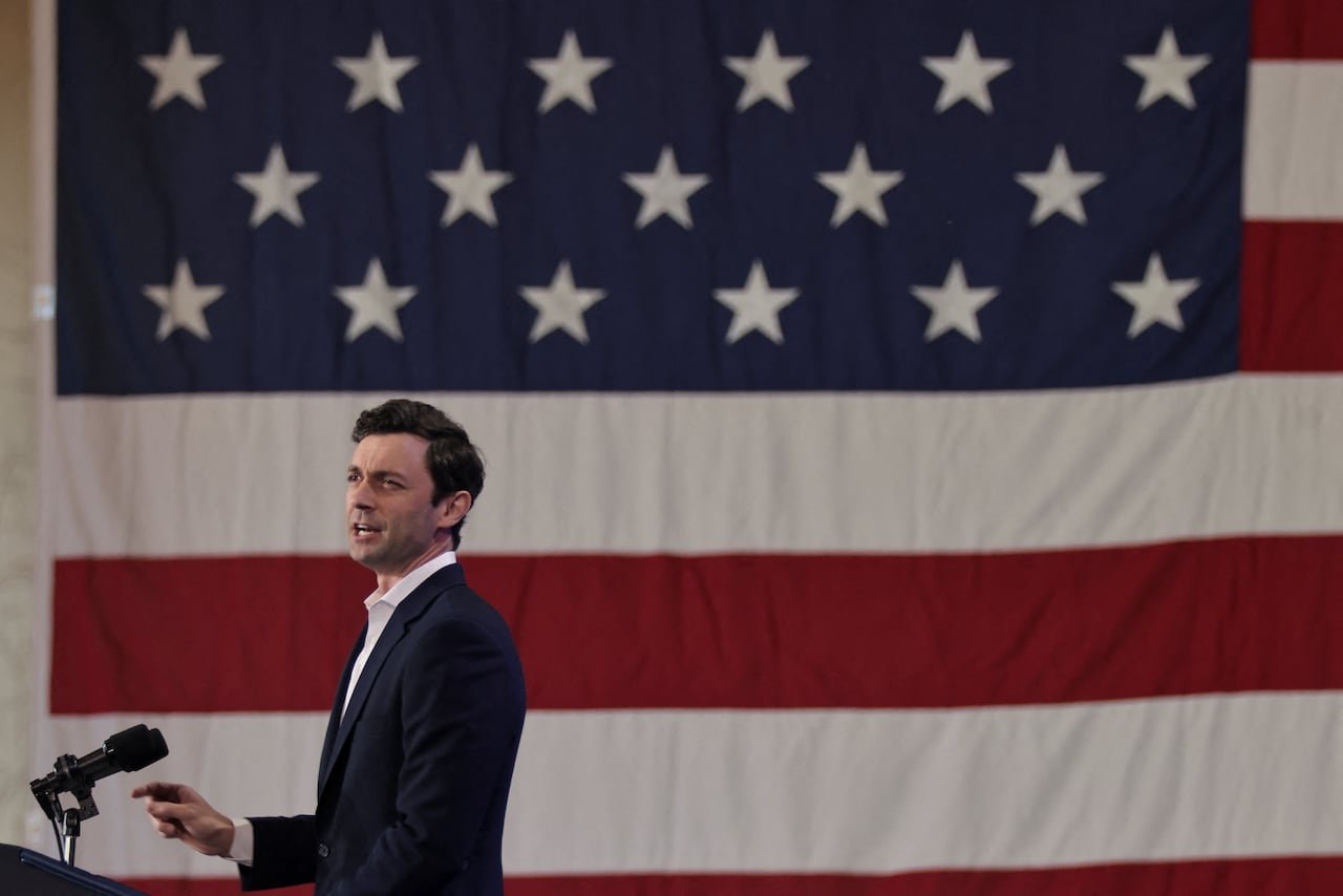 A man at a podium speaks next to a large American flag.